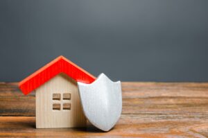 Wooden home figure with protective shield, illustrating the security of owner’s title insurance with Title Resources.