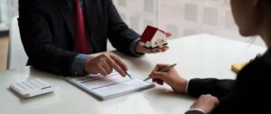 Two people signing a real estate document while holding a model of a home, representing letter reports for property transactions at Title Resources Inc. in Kirkwood, MO